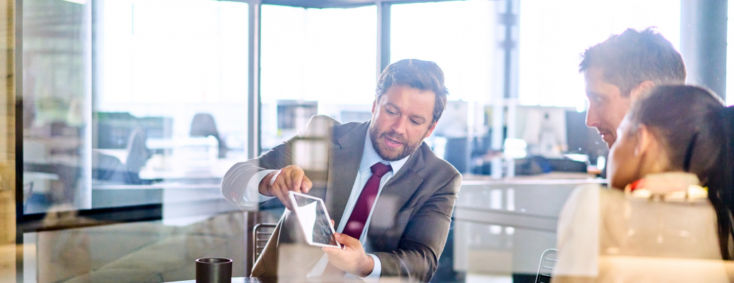 un pofessionnels montre une tablette à ses clients avec lesquels il échange sur leur dossier