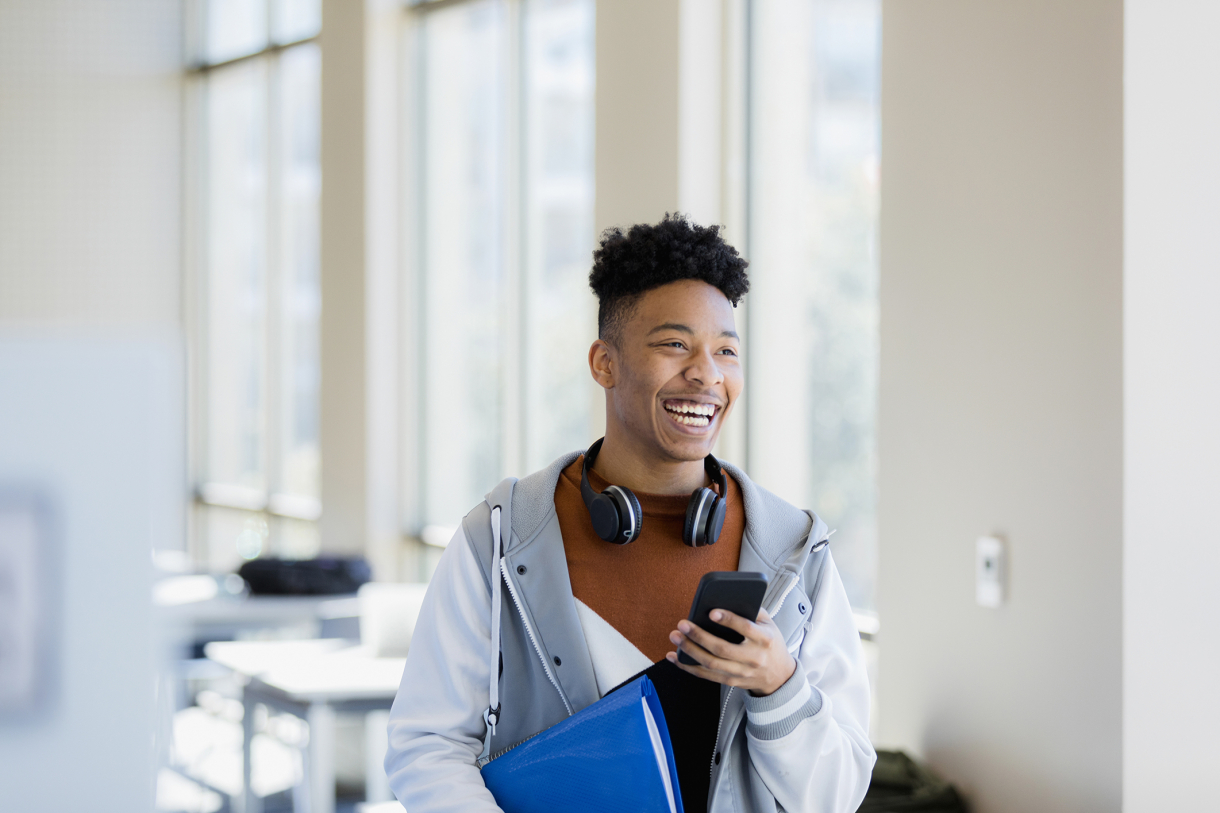 Lycéen avec son téléphone en main et son cahier sous le bras.